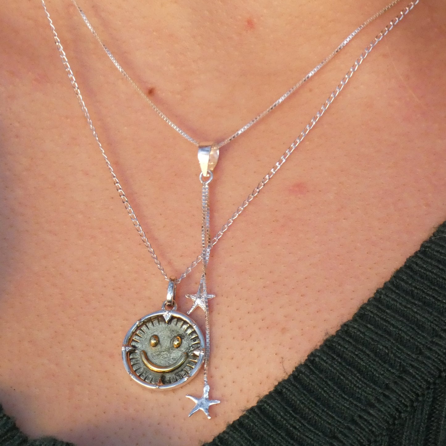 Two silver necklaces with pendants on a person's neck